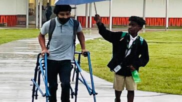 Un alumno de 8º grado protege de la lluvia a un compañero con parálisis cerebral con su paraguas