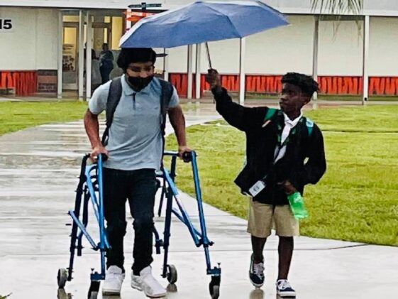 Un alumno de 8º grado protege de la lluvia a un compañero con parálisis cerebral con su paraguas